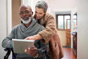 Older couple - man is using a walker, wife looks over his shoulder at tablet