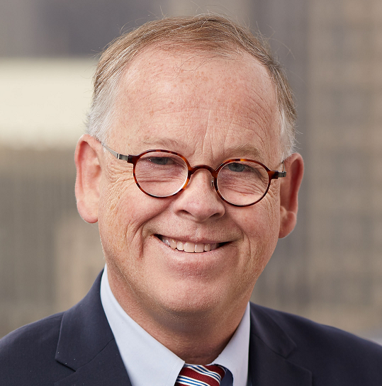 Older man with glasses and salt and pepper hair smiles at camera