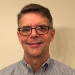 Middle aged man with salt and pepper hair and glasses smiles at camera