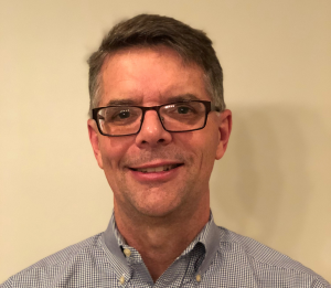 Middle aged man with salt and pepper hair and glasses smiles at camera