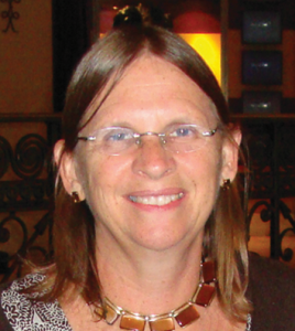 Middle aged woman with shoulder length brown hair and glasses smiles at camera