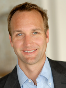 Young man in his thirties with short brown hair smiles at the camera