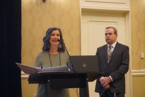 A woman at a podium with a Dell laptop and a white binder and National Disability Institute Executive Director, Thomas Foley, at the 2021 National Conference on Special Needs Planning and Special Needs Trusts